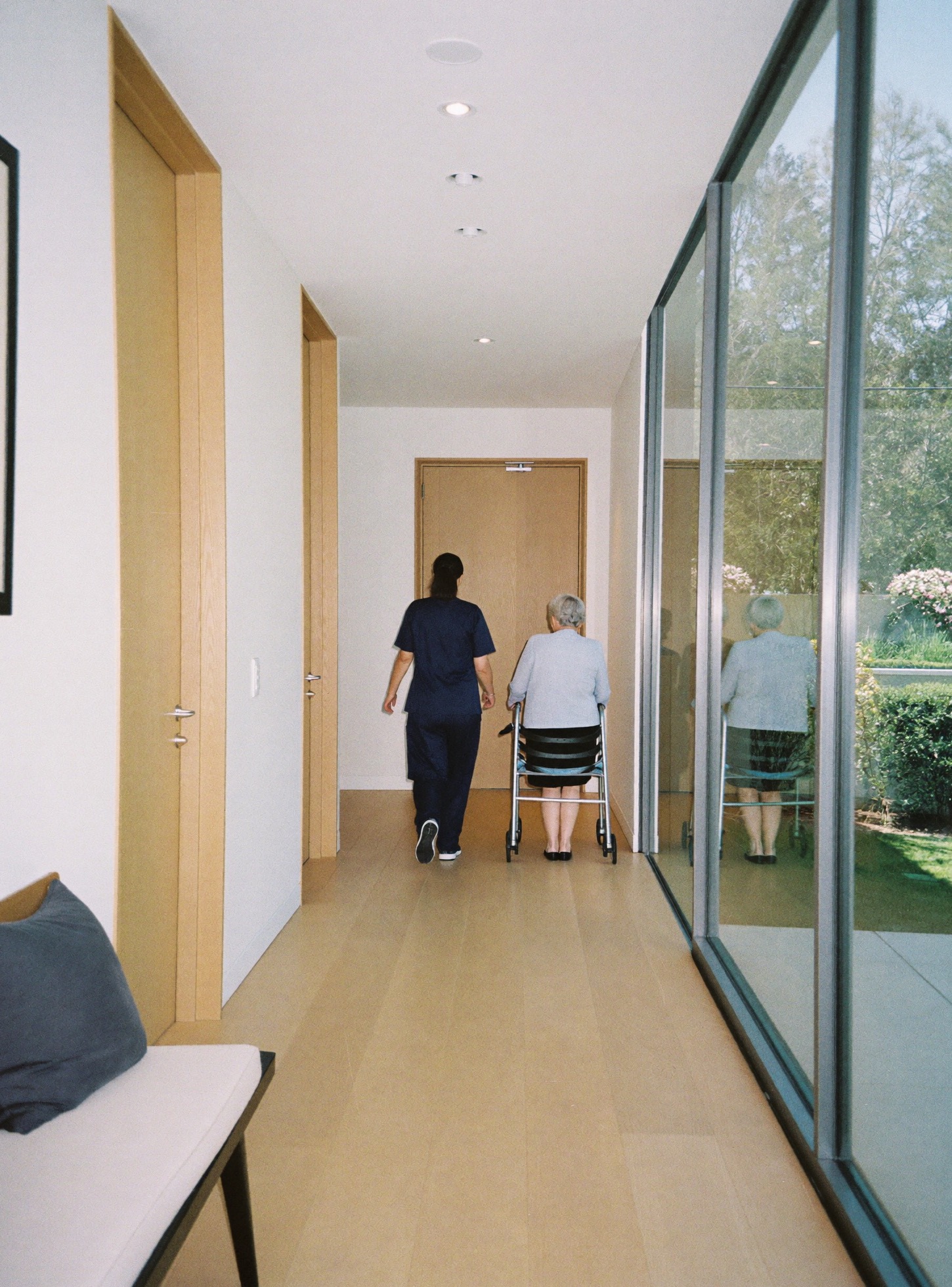 Nurse walking beside a resident with a walker in a care home corridor